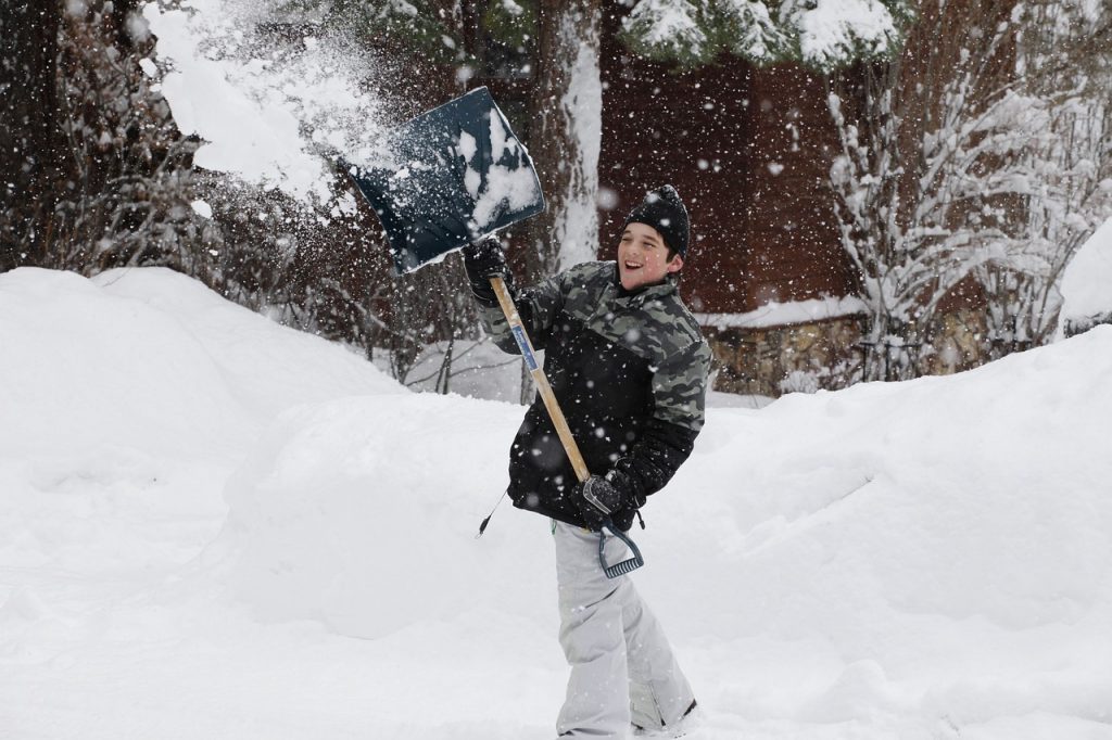 young boy lifting snow shovel over head